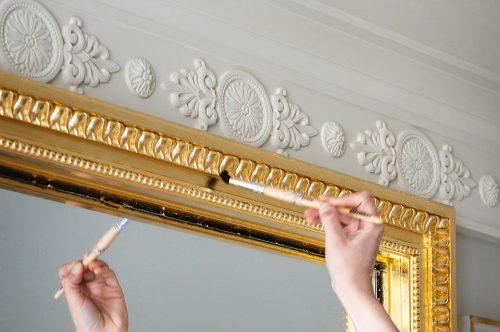 Finalisation de la dorure du cadre d'un miroir.